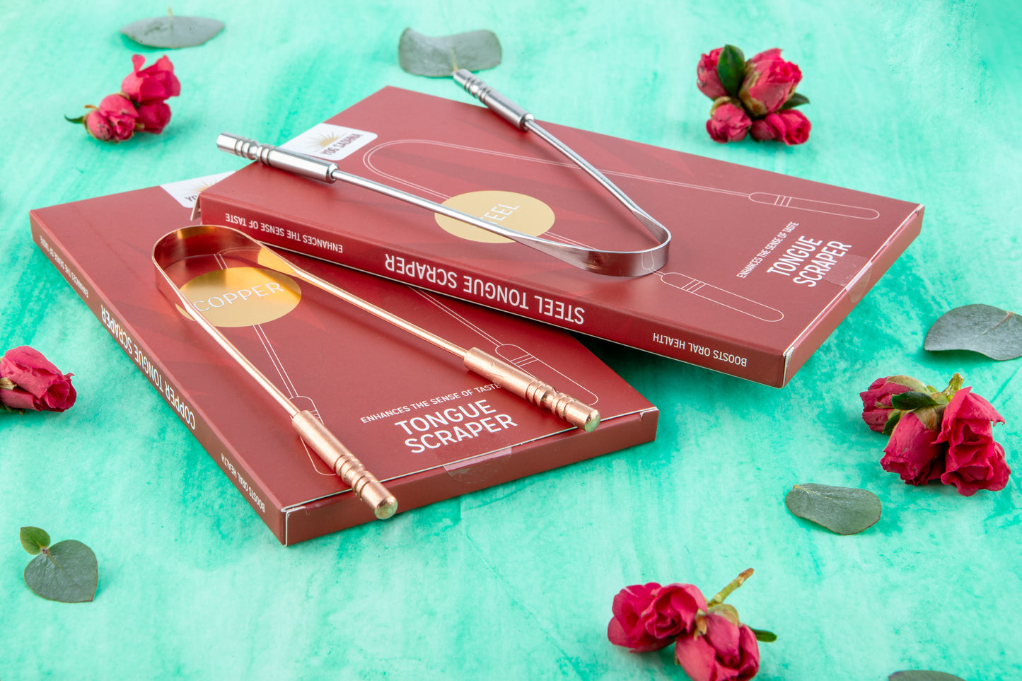 Two tongue scrapers in red packaging on a teal background with flowers