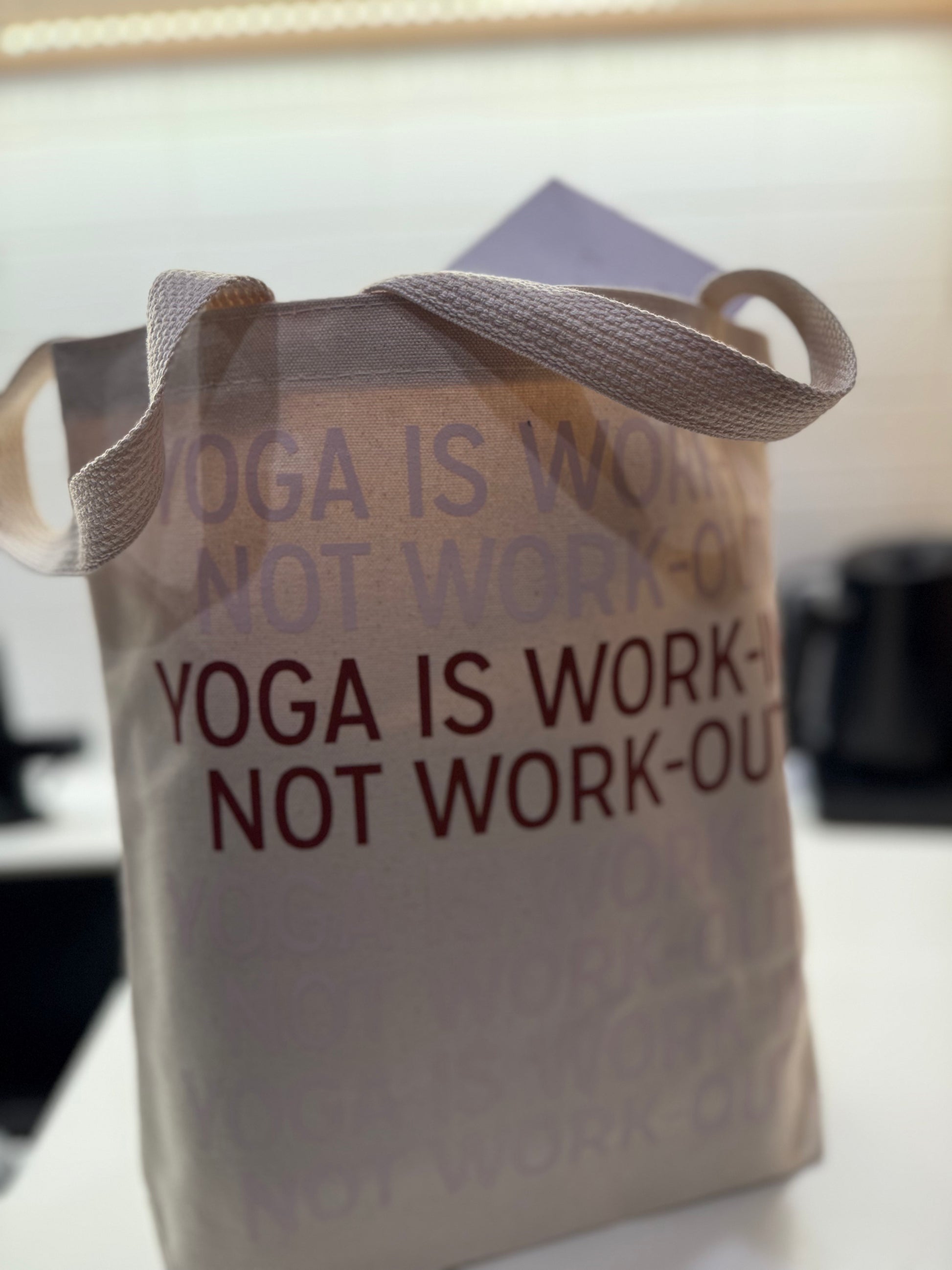Canvas bag with 'Yoga is work, not workout' text on a blurred background